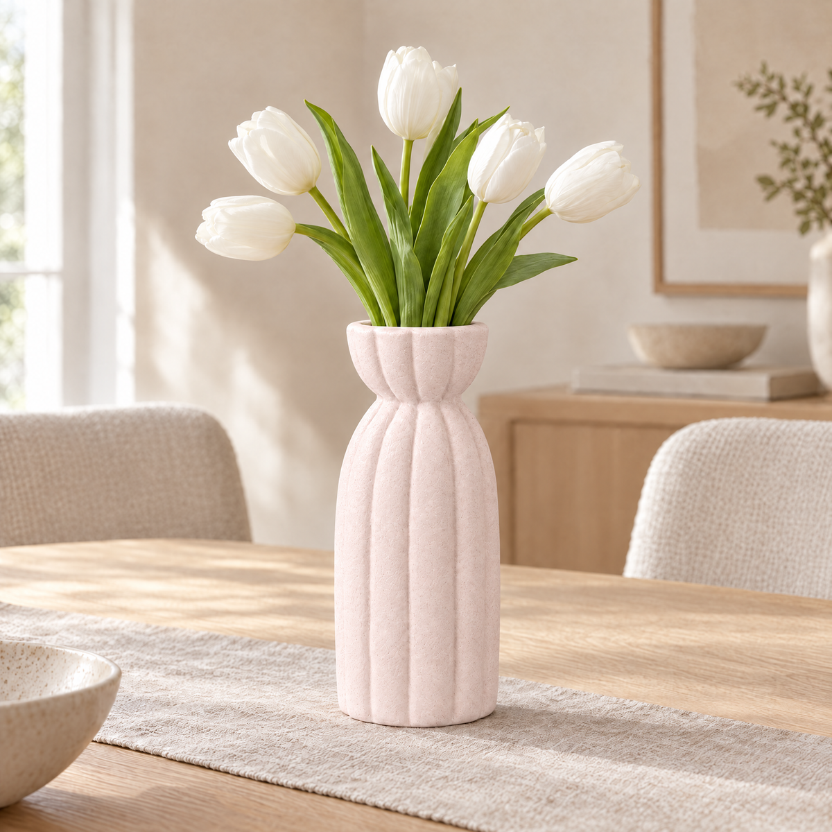 Light pink ribbed stoneware vase with white tulips on a dining table